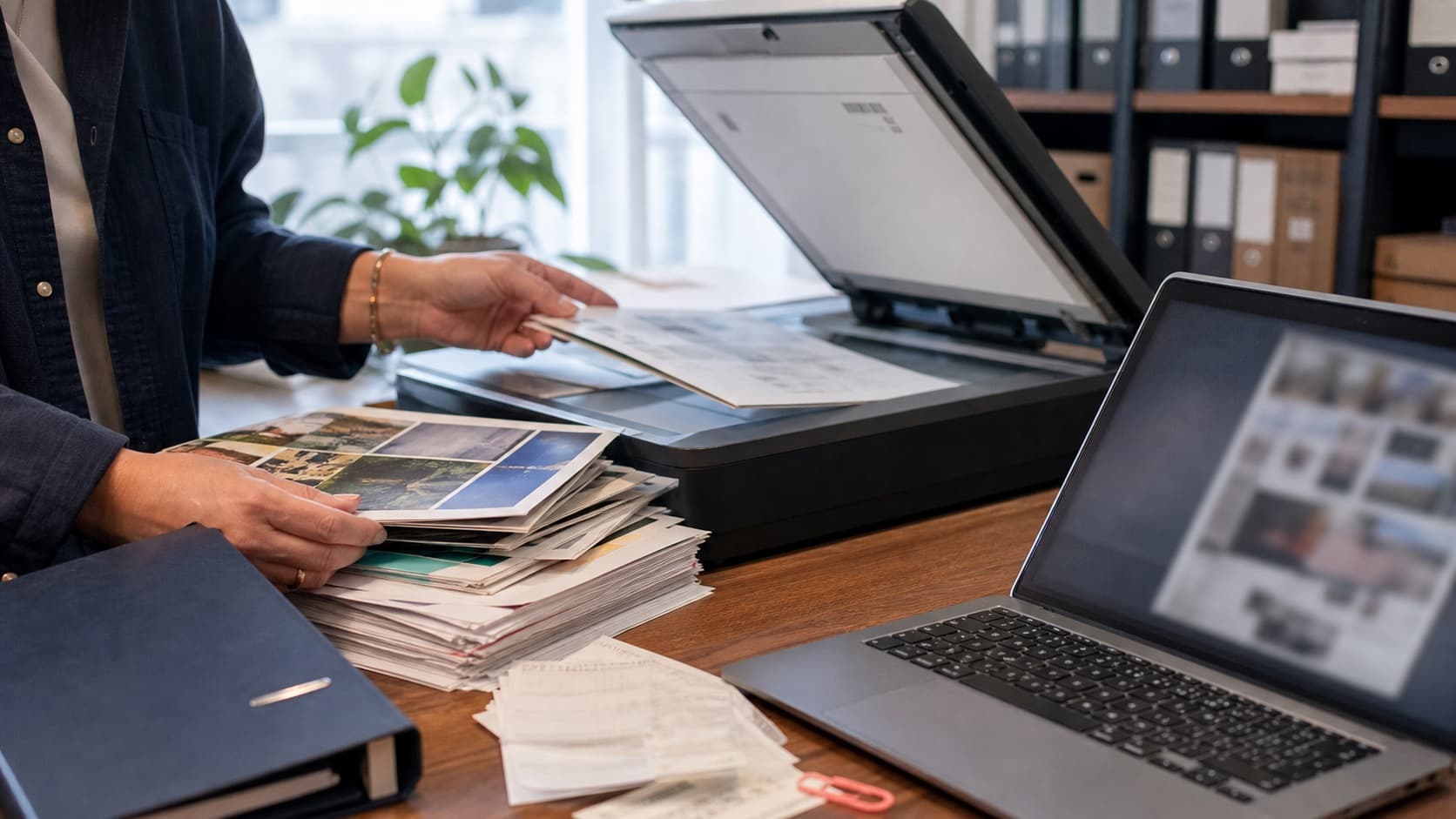Stor bunke fotos og dokumenter scannes ved siden af en computer